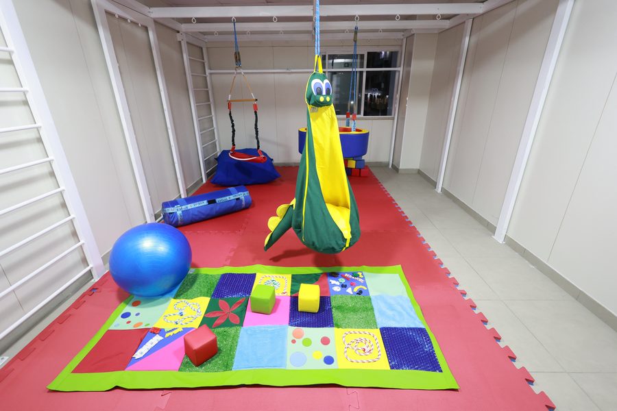 Sala de integração sensorial com balanço suspenso, tatame colorido, bola e escada de parede