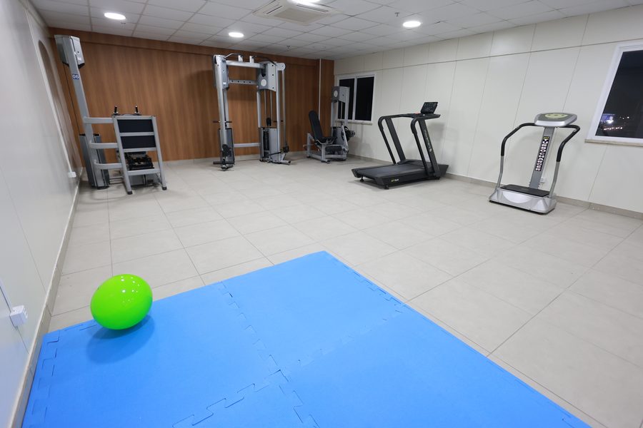 Sala de reabilitação física com aparelhos de musculação, esteira, plataforma vibratória e tatame